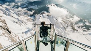 Mann auf gläserner Aussichtsplattform, spektakuläres Bergpanorama, Aussichtsplattform aud Glas, Ausblick auf schneebedeckte Gipfel, Alpenpanorama, Schladming-Dachstein, 